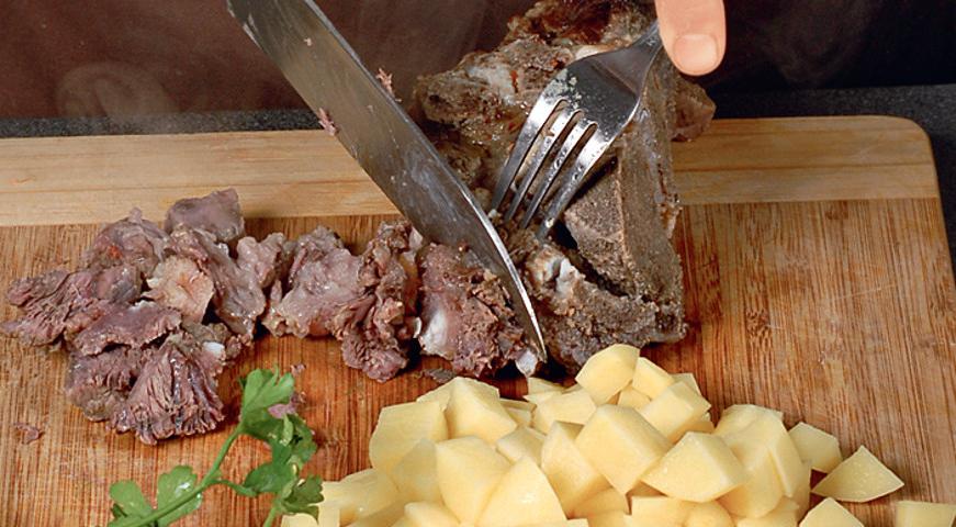 Очистите картофель и нарежьте его небольшими кубиками. Вымойте и измельчите свежую зелень. Чеснок очистите и разомните в чеснокодавилке. Мясо выньте из бульона, отделите от кости и нарежьте на небольшие кусочки. Процедите бульон и верните его на плиту для дальнейшего приготовления.