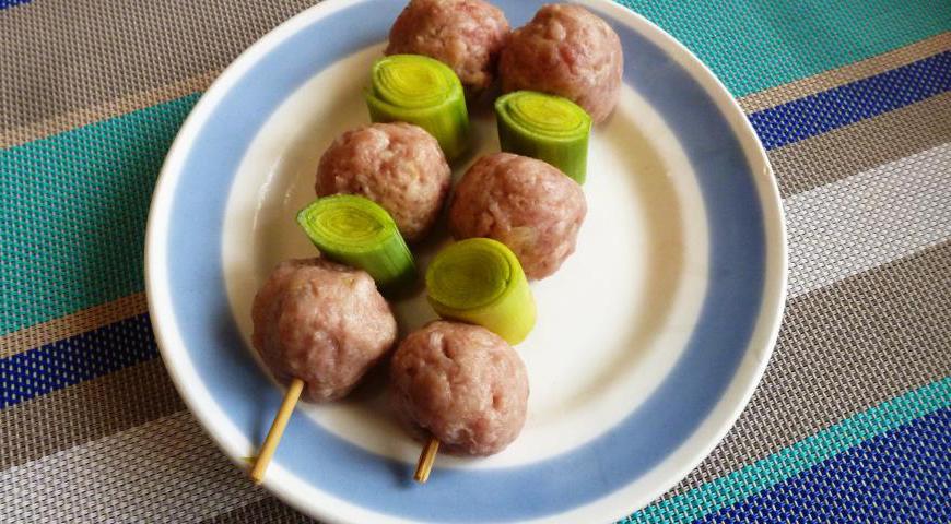 Нарежьте лук-порей на небольшие кусочки. Нанизывайте поочередно фрикадельки и кусочки порея на деревянные шпажки, предварительно замоченные в воде для предотвращения подгорания.