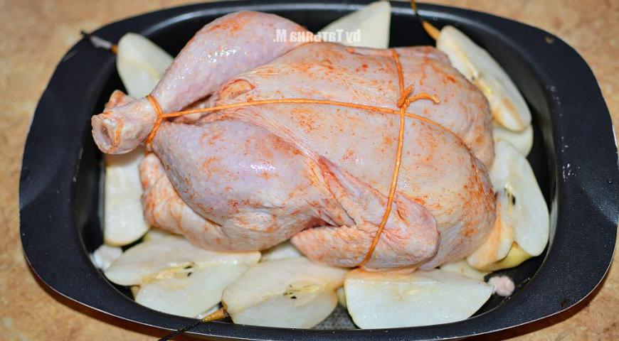 Свяжите ножки и крылья цыпленка жаропрочной кулинарной нитью. Уложите птицу в форму грудкой вверх, рядом разместите дольки оставшихся груш.