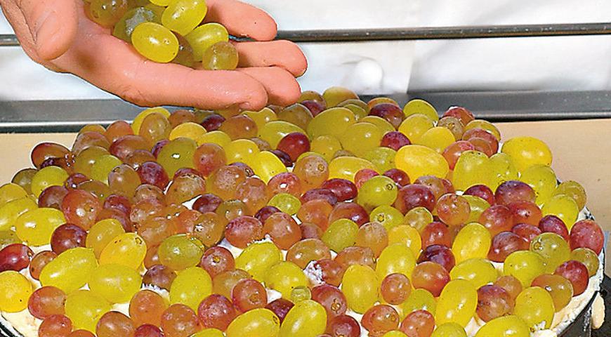 Смажьте поверхность торта оставшимся кремом, украсьте промытыми и обсушенными ягодами винограда. Извлеките торт из формы. Приготовьте глазурь, взбив белок с сахарной пудрой и лимонным соком. Измельчите миндаль и обсыпьте им бока торта, а сверху полейте глазурью.