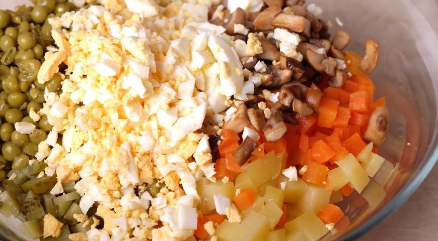 В большой миске объедините картофель, морковь, нарезанные куриные яйца, зелёный горошек, мелко порезанные маринованные огурцы и обжаренные грибы. Добавьте щепотку соли, заправьте постным майонезом и аккуратно перемешайте.