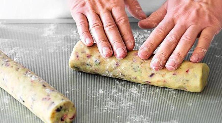 Всыпьте муку в масляную смесь и аккуратно перемешайте. Добавьте вишню, клюкву, изюм, орехи и тыквенные семечки. Хорошо вымесите тесто, затем разделите его на две части. На рабочей поверхности, посыпанной мукой, скатайте из каждой части цилиндры диаметром 5 см и длиной 22 см. Оберните их пищевой пленкой и отправьте в холодильник на 2 часа.