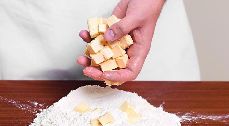 Для теста нарежьте холодное сливочное масло небольшими кубиками. Высыпьте муку на рабочую поверхность горкой, добавьте масло и разотрите руками или порубите ножом до образования крошки.