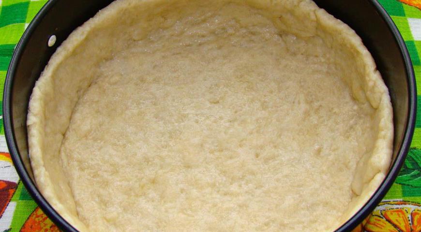 Охлаждённое тесто раскатайте скалкой в пласт нужной толщины и аккуратно выложите его в форму для выпечки, слегка подогнув края. Форму можно предварительно застелить пергаментной бумагой для удобства.
