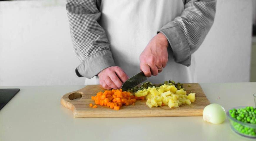 Тщательно вымойте картофель и морковь щеткой. Запеките их в духовке, завернув в фольгу, при температуре 210 °C или сварите в мундире. После приготовления опустите в холодную воду, дайте остыть, очистите и нарежьте небольшими кубиками размером 6 мм. Аналогичным образом подготовьте кальмаров и огурцы, предварительно очистив последних от кожуры, если она слишком жесткая.
